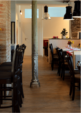 Modernes Esszimmer mit Holztisch, schwarzen Stühlen und Stehleitern, beleuchtet von großen Pendelleuchten.