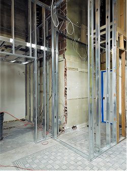 Innenraum einer Baustelle mit Metallrahmenkonstruktion und unvollständiger Wand neben gepflastertem Boden.