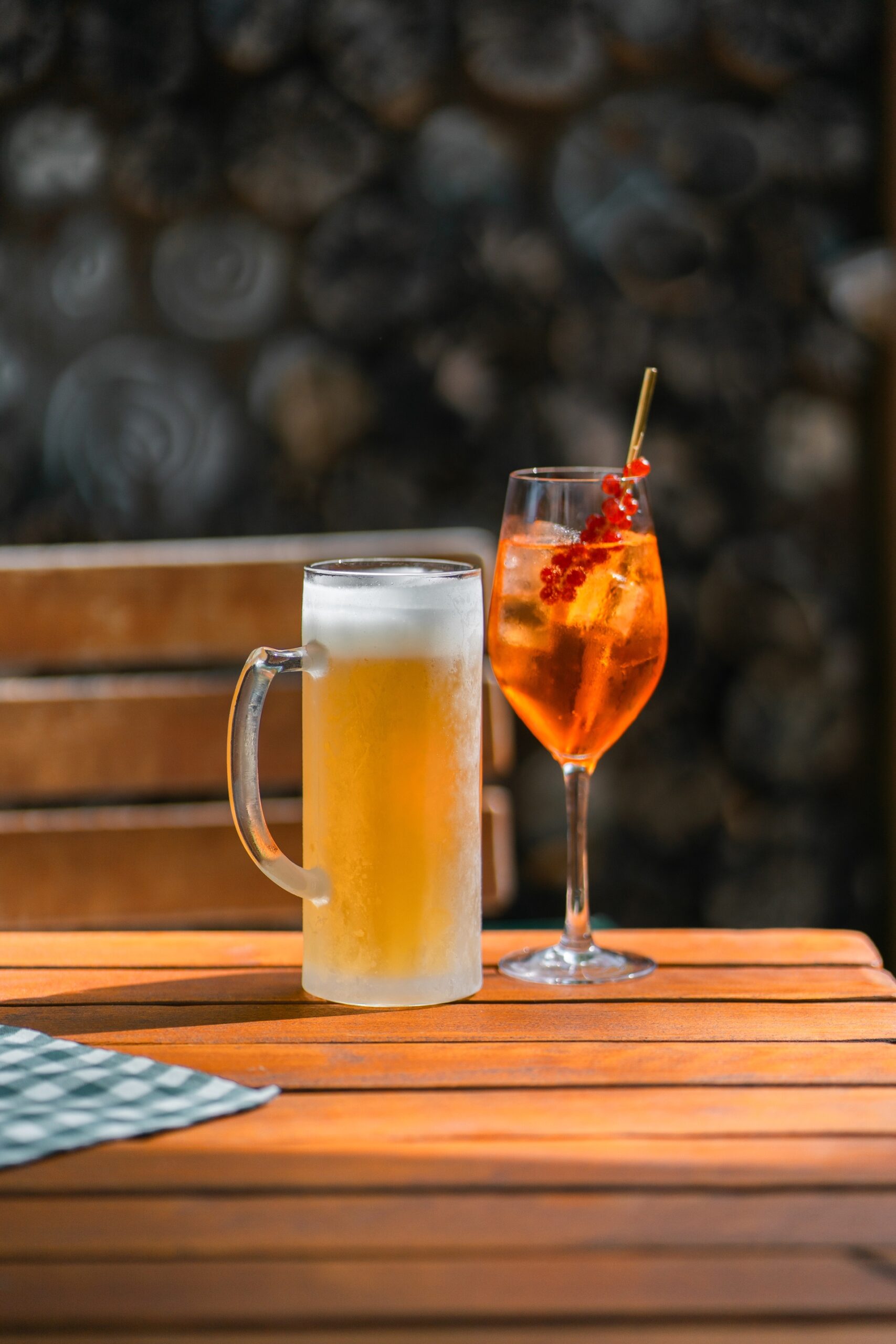 Zwei Gläser mit Getränken auf einem Holztisch: ein Bier und ein orangefarbener Cocktail mit roten Beeren.