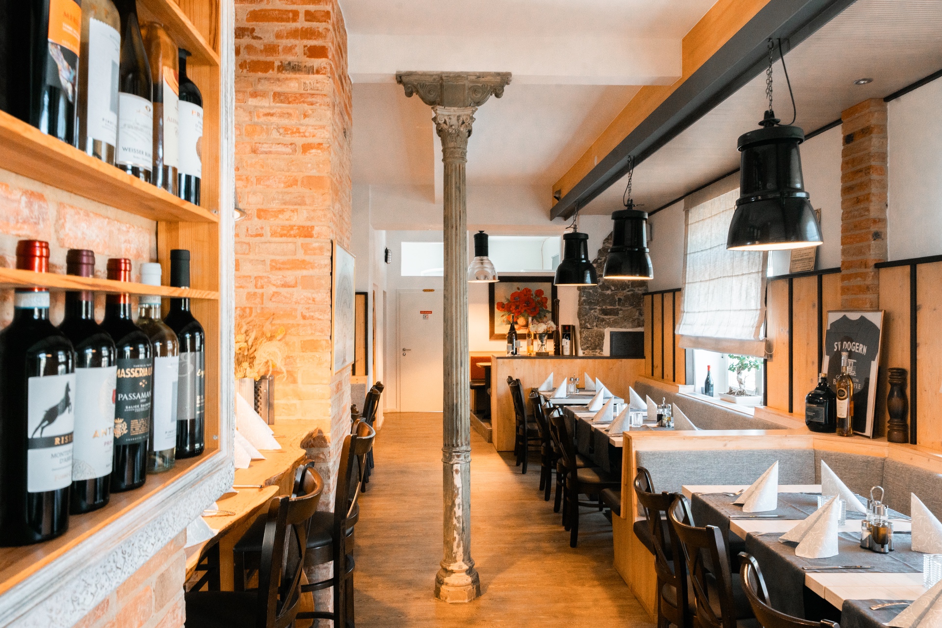 Gemütliches Restaurant mit Holzmöbeln, Weinfregatten und dekorativen Lampen, das eine einladende Atmosphäre bietet.