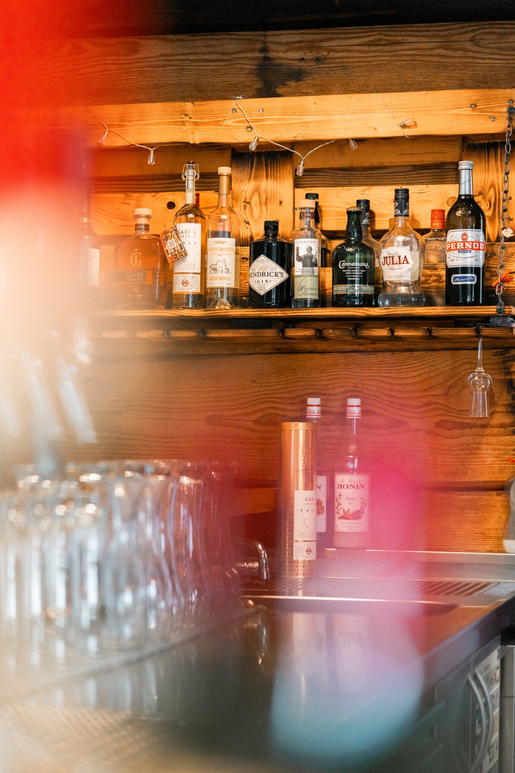 Regal mit Flaschen alkoholischer Getränke in einer Bar, darunter Gin, Wodka und Liköre; Gläser im Vordergrund.