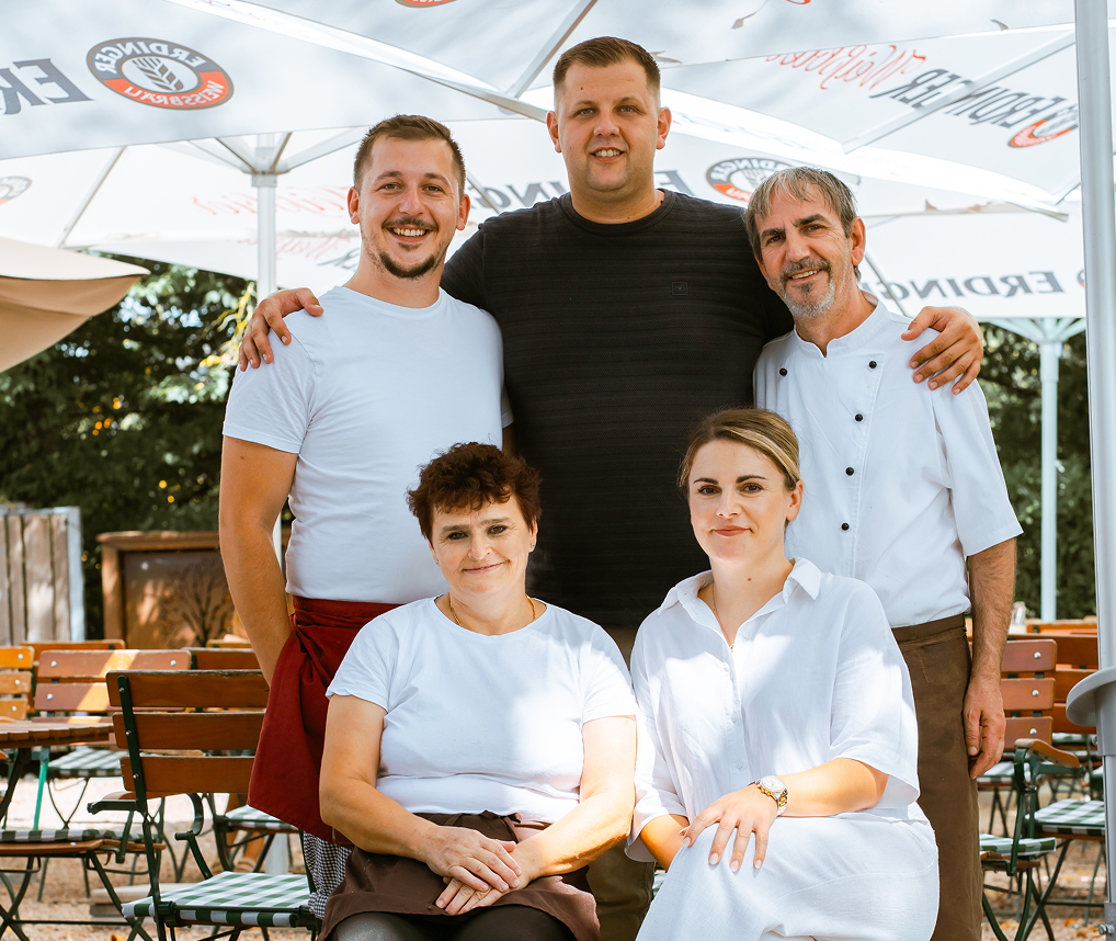 Fünf Personen in Arbeitskleidung posieren lächelnd unter Sonnenschirmen in einem Außenbereich.